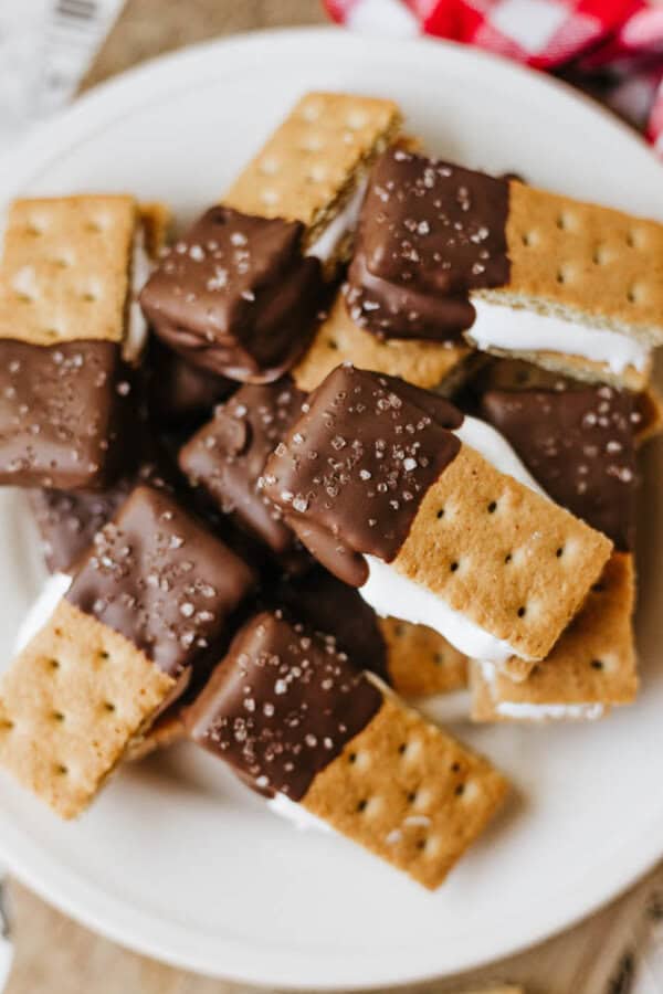 A plate of 3-ingredient S'mores Bites: rectangular graham cracker sandwiches filled with white marshmallow, partially dipped in chocolate, and sprinkled with coarse sea salt.