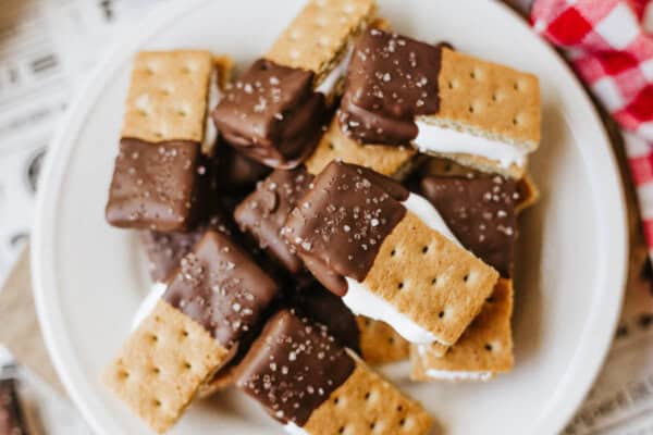 A plate of 3-ingredient S'mores Bites made with graham crackers, marshmallow filling, and edges dipped in chocolate, sprinkled with coarse sugar on top.