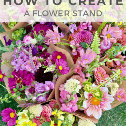 Bouquets of colorful flowers, including pink, yellow, and purple blooms, wrapped in brown paper are displayed outdoors on green grass. Text overlay reads, โHow to Create a Flower Stand.โ.