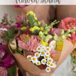 A bouquet of colorful flowers wrapped in brown paper sits on a table surrounded by other flower arrangements. Text reads โOUR FREE LITTLE flower standโ and โhomemadeheather.com.โ.
