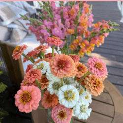 A jar of vibrant pink, orange, and white flowers sits on a wooden table outdoors. Text reads: Cut Flower Garden First Year Tour and homemadeheather.com.